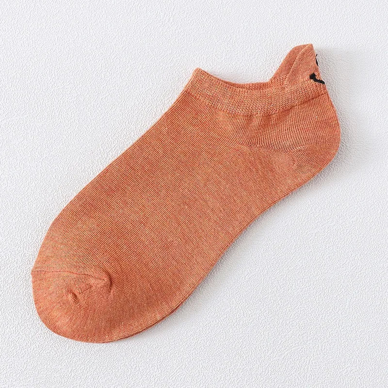 Un par de calcetines anaranjados quemados con textura de punto y un pequeño bordado de cara sonriente negra.