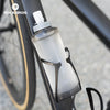 Una botella de agua deportiva de silicona transparente con tapa blanca, unida a un cuadro de bicicleta.