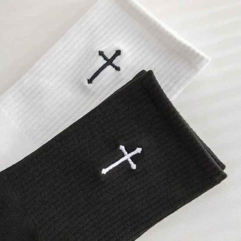 A pair of black mid-length cotton socks with a white cross pattern lying on a white surface.
