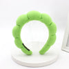A lime green sponge terry cloth headband for hair styling displayed on a white circular stand.
