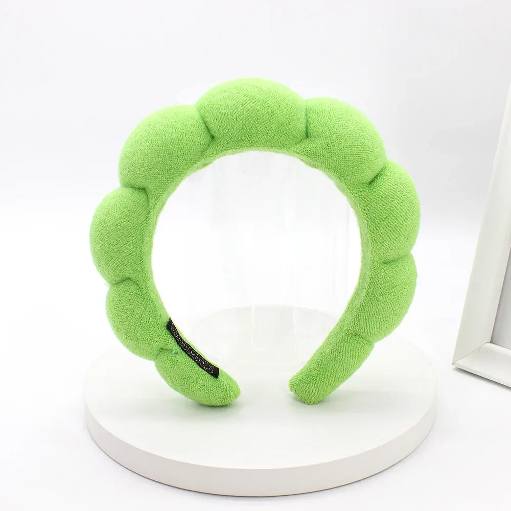A lime green sponge terry cloth headband for hair styling displayed on a white circular stand.