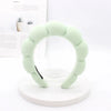 A light green sponge terry cloth headband for hair styling displayed on a white circular stand.