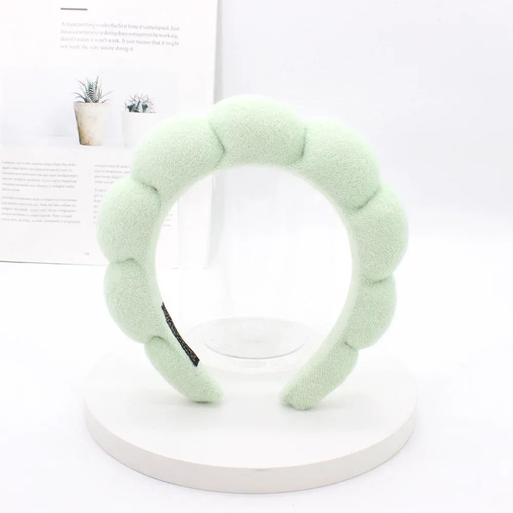 A light green sponge terry cloth headband for hair styling displayed on a white circular stand.