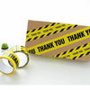 A roll of yellow and black industrial safety warning tape is shown next to a cardboard box.