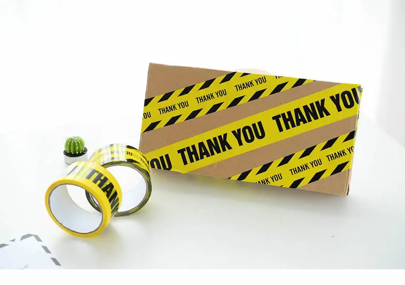A roll of yellow and black industrial safety warning tape is shown next to a cardboard box.