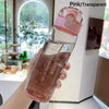 A hand holds a pink transparent sports water bottle filled with water in a bright indoor setting.