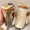 A silver thermo mug with a white lid and gold display, next to a beige insulated travel cup.