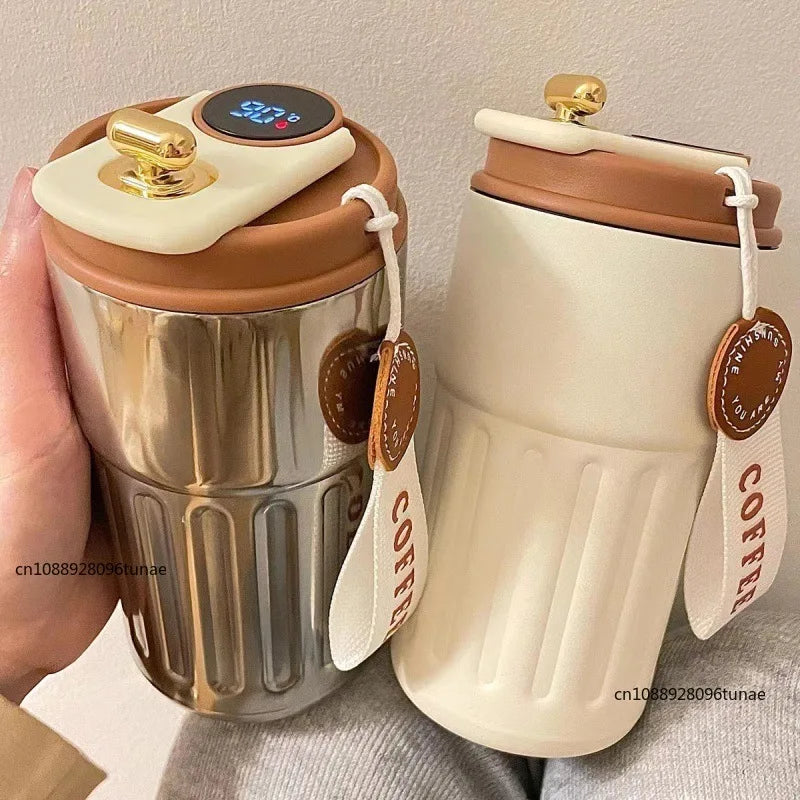 A silver thermo mug with a white lid and gold display, next to a beige insulated travel cup.