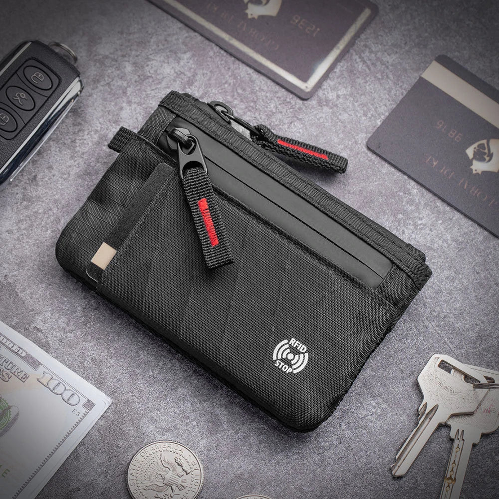 A black slim RFID blocking wallet is shown lying on a gray surface with various cards and keys nearby.