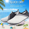 A pair of gray and black slip-on aqua socks shown against a bright blue sky and ocean background.