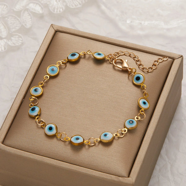 Gold charm bracelet featuring blue and white evil eye beads set in a rectangular box.