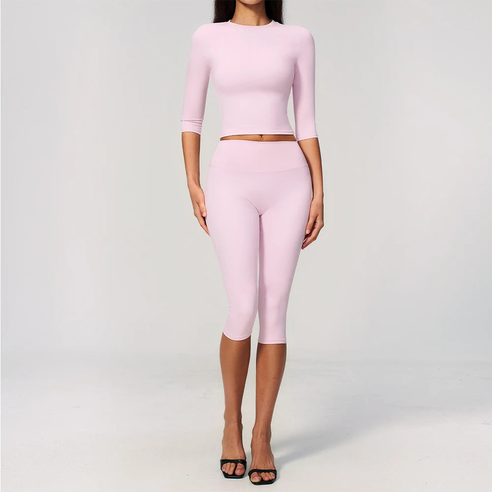 A woman models a light pink yoga and fitness leggings set consisting of a long-sleeved top and matching leggings.