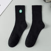 A pair of black men's athletic crew socks with a green embroidered logo on the ankle.