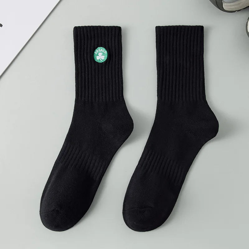 A pair of black men's athletic crew socks with a green embroidered logo on the ankle.