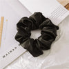 A black satin scrunchie tied in a voluminous, ruched style resting on white paper.