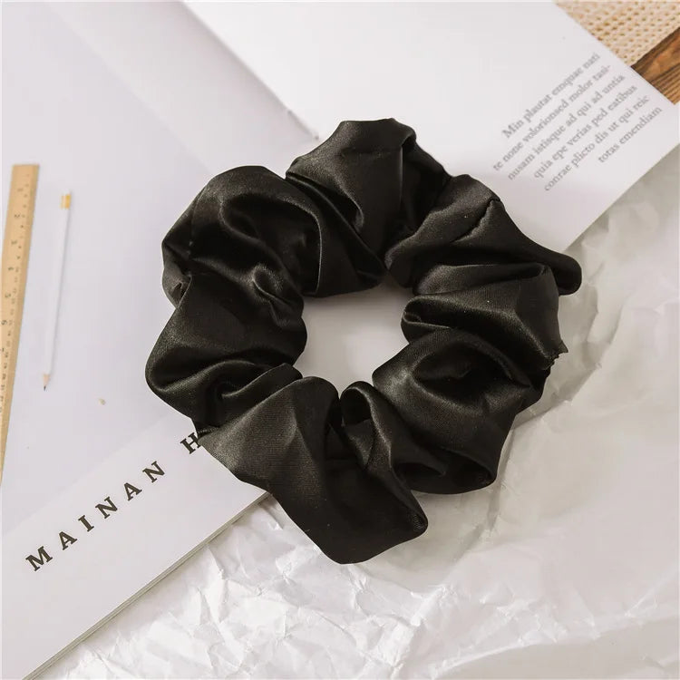 A black satin scrunchie tied in a voluminous, ruched style resting on white paper.