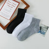 Ein Stapel schwarzer, weißer und grauer Baumwoll-Socken für Herren mit offenem Schaft neben einem Buch.
