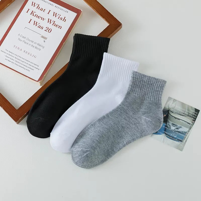 Ein Stapel schwarzer, weißer und grauer Baumwoll-Socken für Herren mit offenem Schaft neben einem Buch.