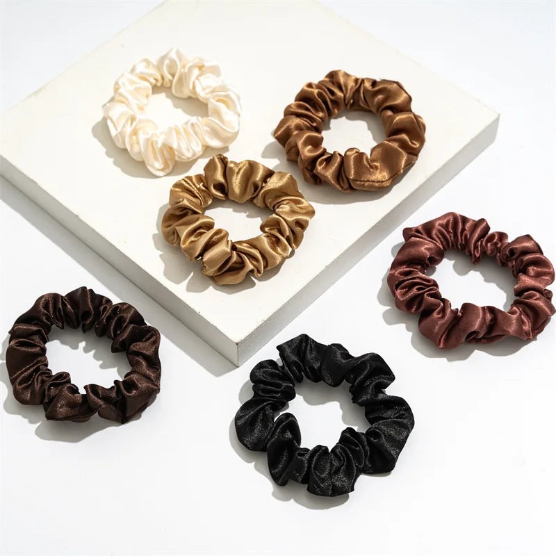 A collection of satin scrunchies in various shades of gold, bronze, and black arranged on a white surface.
