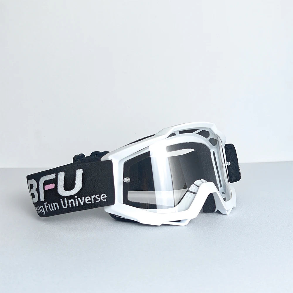 A pair of white and black sport-grade skiing goggles with a clear lens resting on a gray surface.