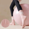 Un par de calcetines de yoga y pilates rosas antideslizantes puestos por una persona junto a una gran pelota de ejercicio ros