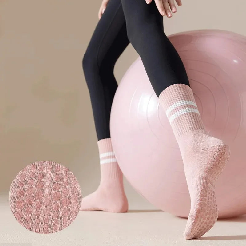 Un par de calcetines de yoga y pilates rosas antideslizantes puestos por una persona junto a una gran pelota de ejercicio ros