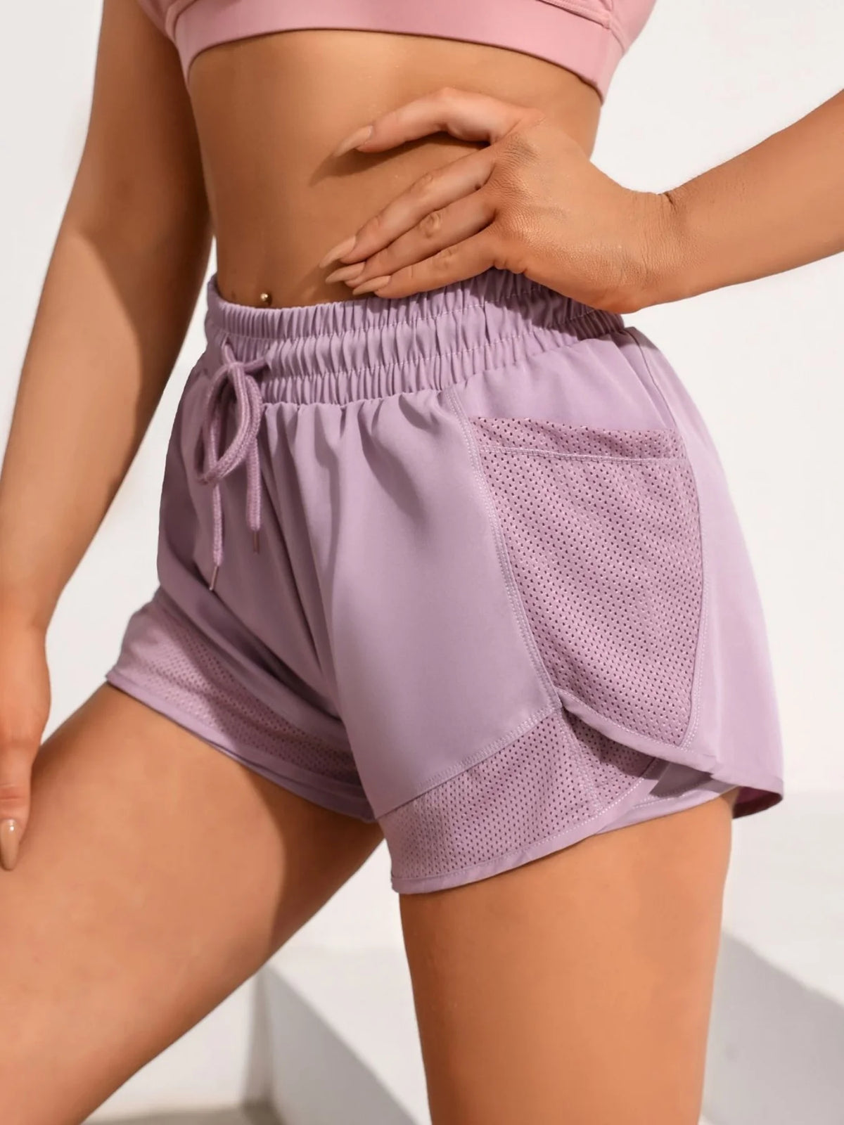 A model wears light purple athletic shorts with mesh pockets and a matching crop top.