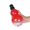 Eine Hand hält eine rote, kürbisförmige Sportflasche mit schwarzem Deckel und Tragegurt.