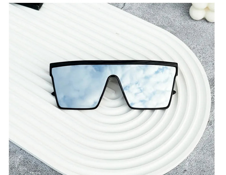 Pair of black-framed retro square sunglasses with reflective blue lenses resting on a white, wavy surface.