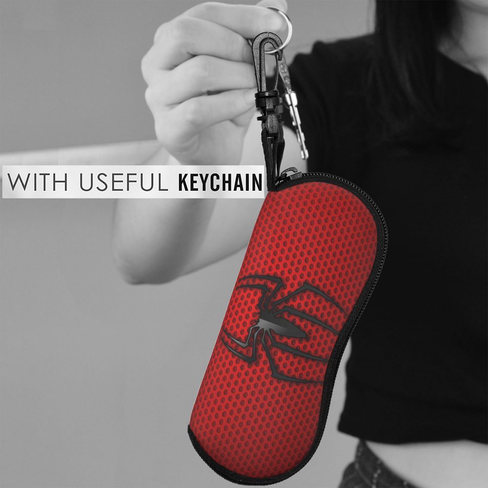 A hand holds a red spider web shaped keychain pouch with a metal keyring against a gray background.