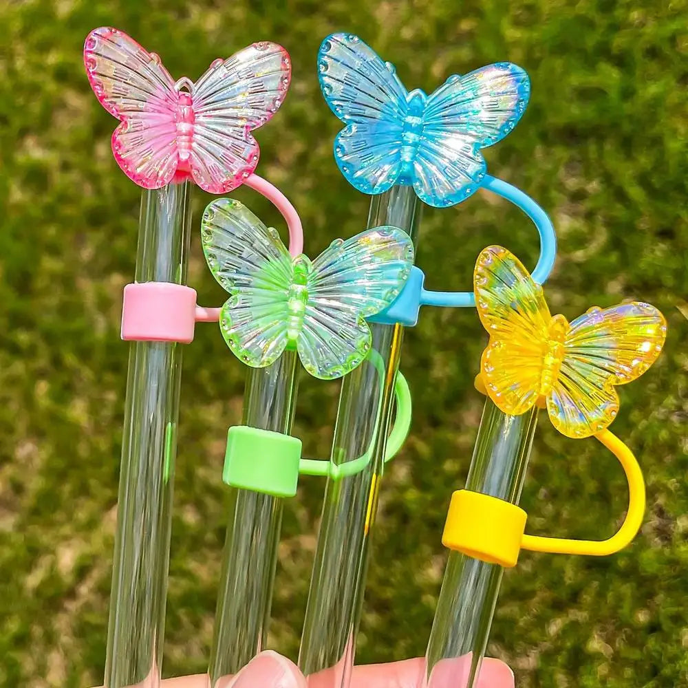A collection of colorful silicone butterfly straw covers on clear straws against a green outdoor background.