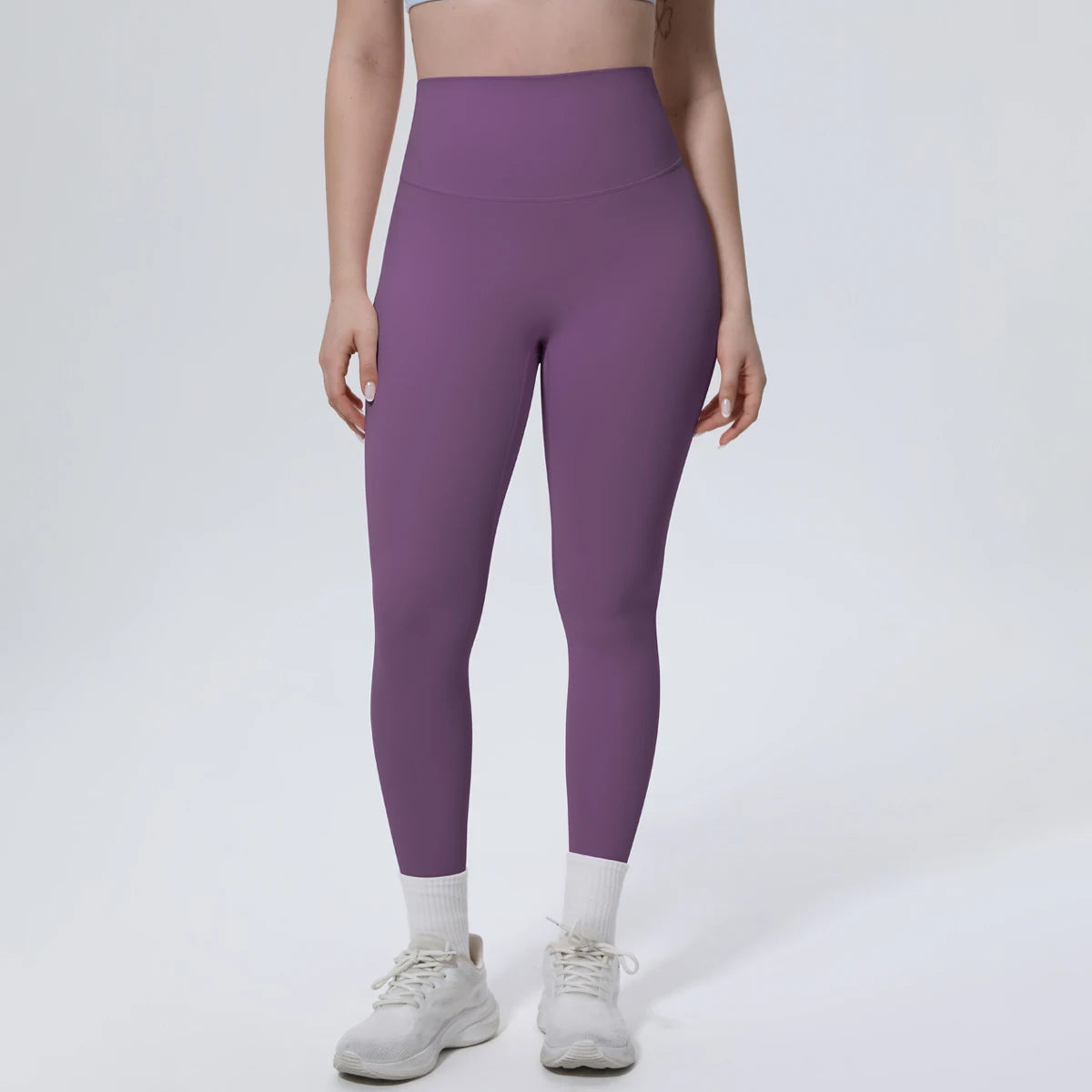 A model is wearing purple high-waisted quick-drying yoga and fitness leggings with white socks and white athletic shoes.