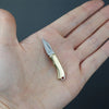 Un pequeño cuchillo llavero plegable de latón sostenido en una mano humana abierta.