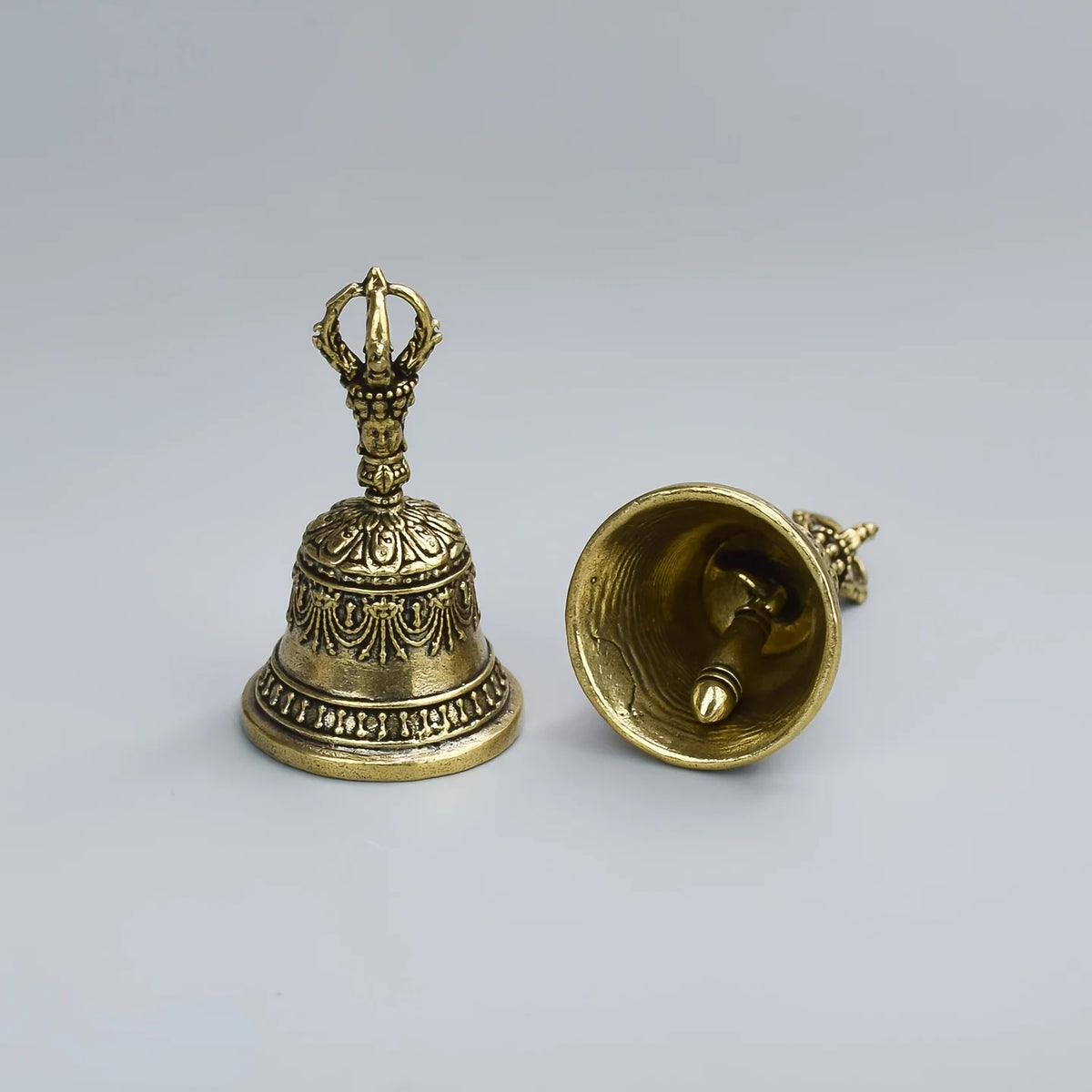 Cloche de bronze à shaker avec sommet orné et cloche évasée, présentée sur fond gris clair.
