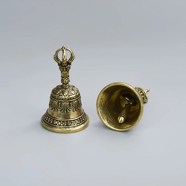 A hand-held bronze bell shaker with an ornate top and a flared bell, displayed against a light gray background.