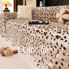 A plush leopard print sofa cover blanket with cream and brown tones is displayed on a light floor.