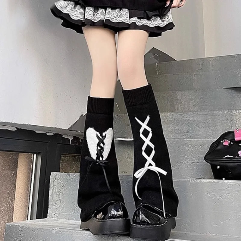 A person wearing black Gothic Lolita heart bow leg warmers and black shoes standing on outdoor stairs.