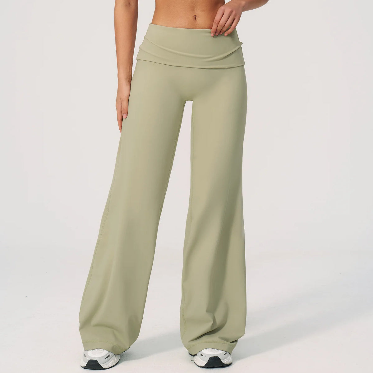 A model wearing olive green flared high-waist yoga pants and white sneakers.