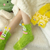 A pair of bright green plush caterpillar floor socks lying on a white fluffy blanket.