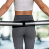 A person wearing a gray sports bra and leggings is demonstrating an adjustable pelvic support hip belt for lower back relief.