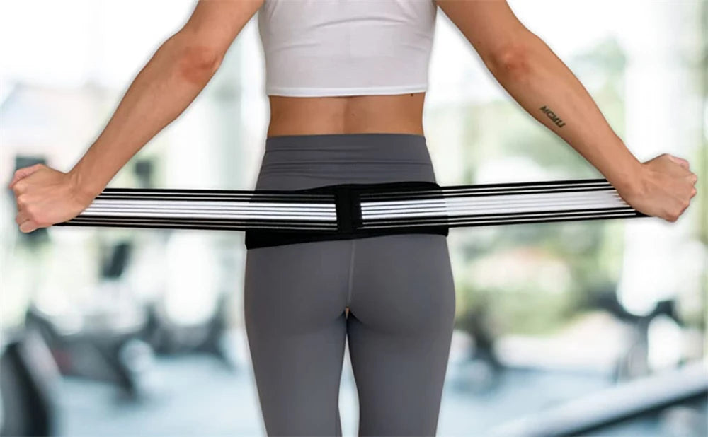 A person wearing a gray sports bra and leggings is demonstrating an adjustable pelvic support hip belt for lower back relief.
