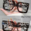 A pair of tortoiseshell patterned rectangular reading glasses shown being held by a hand.