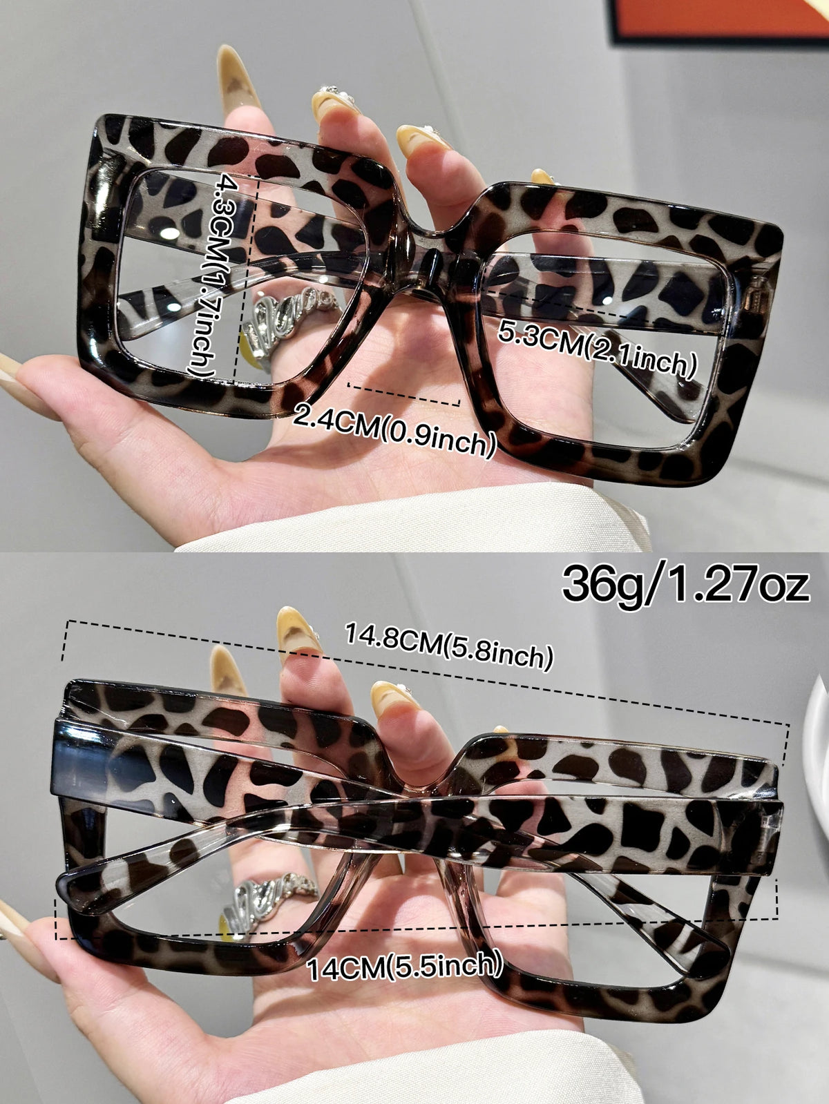 A pair of tortoiseshell patterned rectangular reading glasses shown being held by a hand.