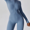 Model trägt einen langärmeligen, figurbetonten blauen Yoga-Jumpsuit mit Zipverschluss.