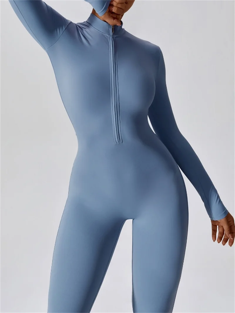 Model trägt einen langärmeligen, figurbetonten blauen Yoga-Jumpsuit mit Zipverschluss.