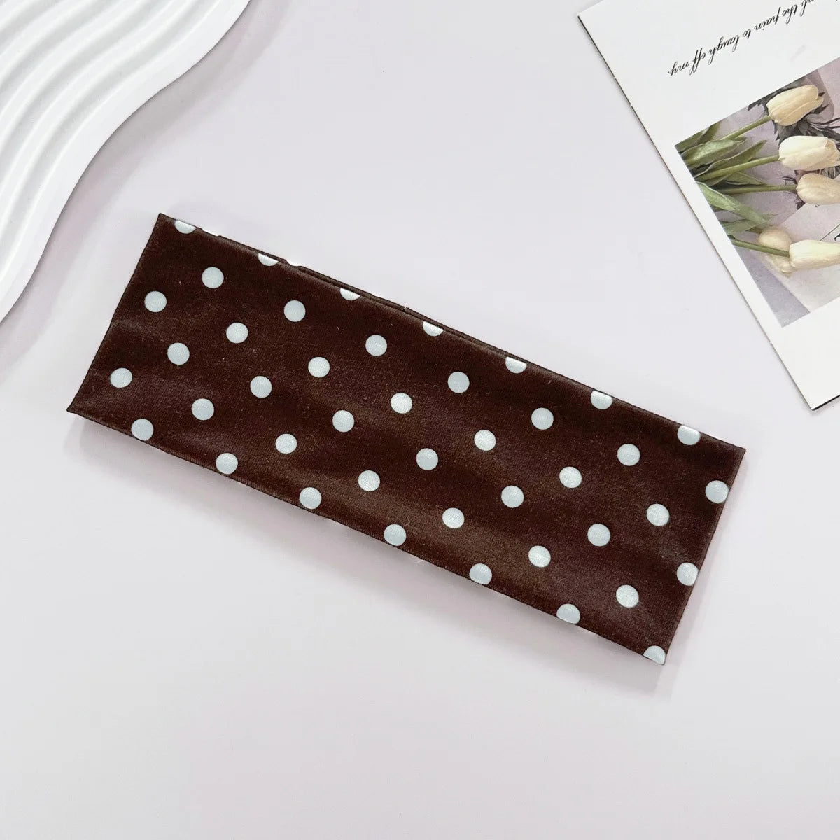 Un bandeau de yoga élastique à pois brun foncé posé sur une surface blanche.