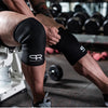 A person wearing black neoprene knee pads while performing a lift in a gym setting.