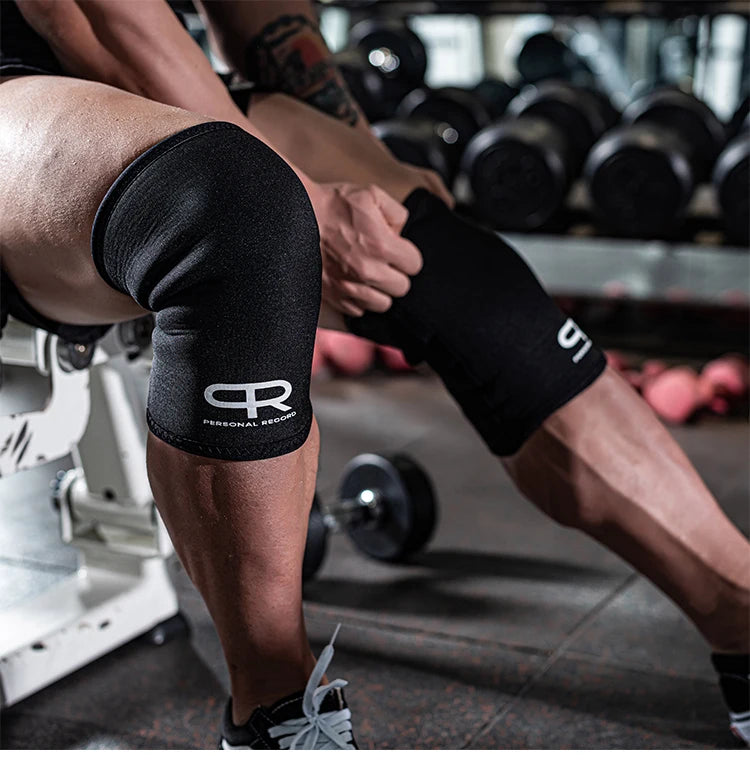 A person wearing black neoprene knee pads while performing a lift in a gym setting.