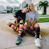 Two young women wearing colorful compression elastic socks sitting on a concrete sidewalk.