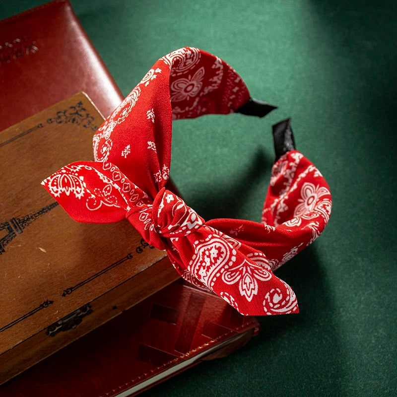 Accesorio de cabello de tela estampada roja atado en un lazo sobre una caja de madera.